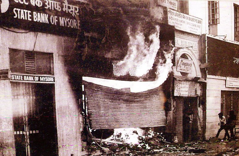 ਸਟੇਟ ਬੈਂਕ ਆਫ਼ ਮੈਸੂਰ ਨਾਲ ਲਗਦੀ ਦੁਕਾਨ ਵਿਚੋਂ ਅੱਗ ਦੇ ਭਾਂਬੜ ਨਿਕਲਦੇ ਹੋਏ। ਨਾਲ ਹੀ ਦਿਸ ਰਹੇ ਸਿੱਖ ਵਿਰੋਧੀ ਲੋਕ ਦੂਜੀ ਦੁਕਾਨ ਨੂੰ ਨੁਕਸਾਨ ਪਹੁੰਚਾਉਣ ਦੀ ਕੋਸ਼ਿਸ਼ ਵਿਚ।